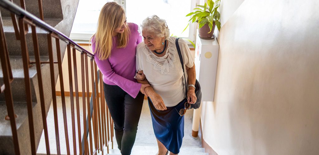Female-caregiver-assisting-senior-woman-climbing-the-stairs