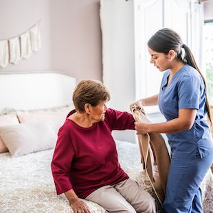 Home caregiver assisting a senior woman to get clothed in a nursing home Home caregiver assisting a senior woman to get clothed in a nursing home