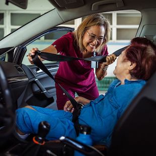 Home caregiver helping elderly patient get seated in passenger seat of parked car Home caregiver helping elderly patient get seated in passenger seat of parked car