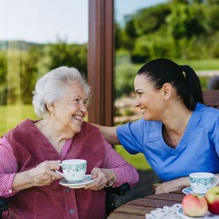 Female caregiver spending time with elderly woman, drinking coffee and talking. Nurse and senior woman in wheelchair enjoying a warm day outdoors. Female caregiver spending time with elderly woman, drinking coffee and talking. Nurse and senior woman in wheelchair enjoying a warm day outdoors.